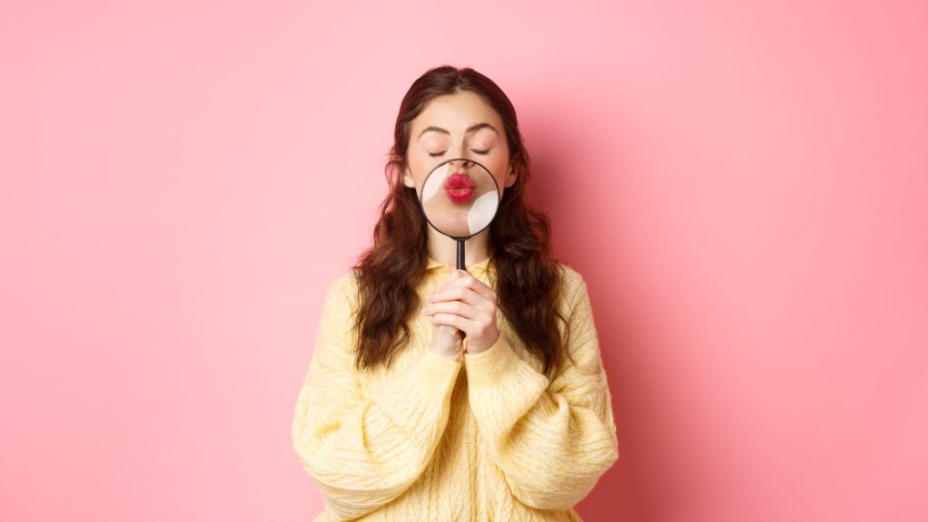 cute-romantic-young-woman-magnify-her-lips-with-magnifying-glass-making-kissing-face-standing-with-closed-eyes-against-pink-background-1-1024x576.jpg